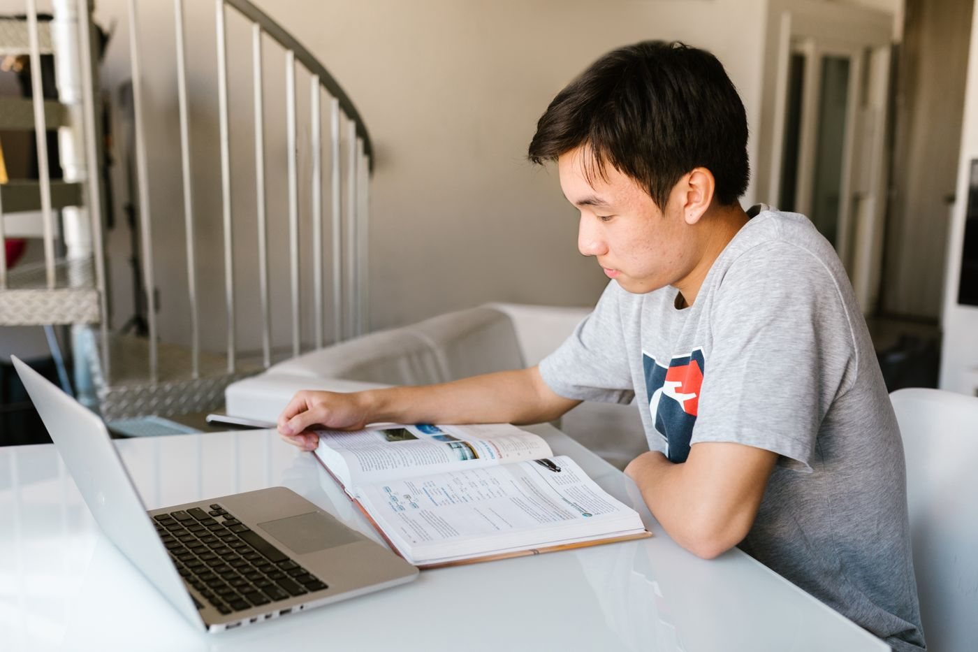 A teenage student working from a textbook beside his laptop