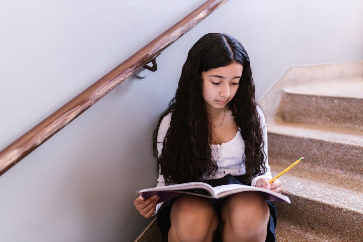 A teenage girl reading and annotating a book on her own