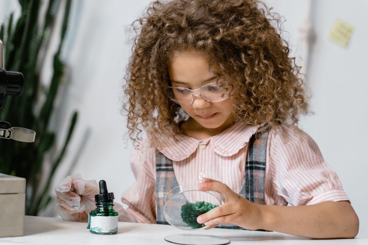 A young girl in safety glasses examining a sample in a petri dish at home